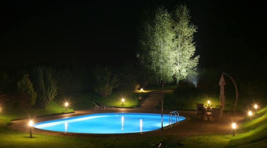 A pool and garden at night, lit by outdoor lights.