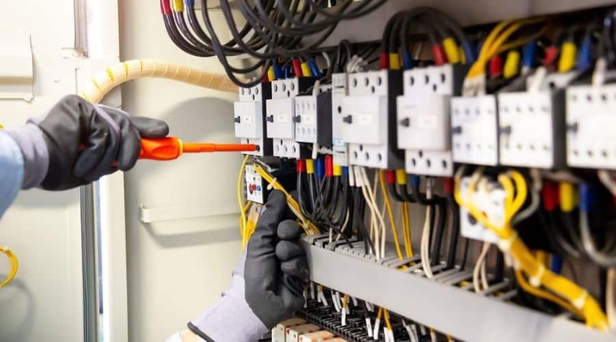 An electrician wearing gloves working on connecting wires in an electrical system.
