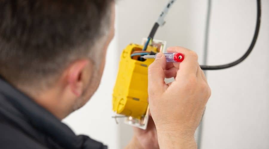 A man using a screwdriver in an electrical junction box