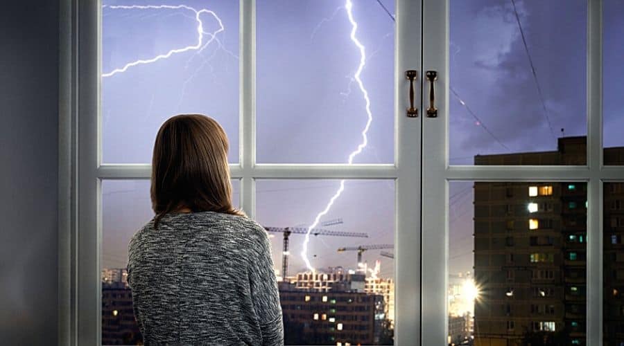 A woman watching a thunderstorm in a city from her window