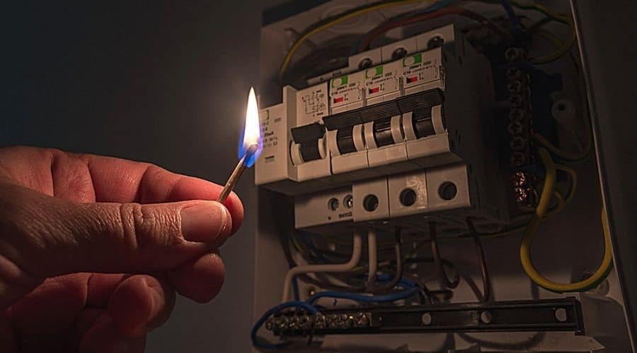 A person holding a lit match to investigate their fuse box during a power outage