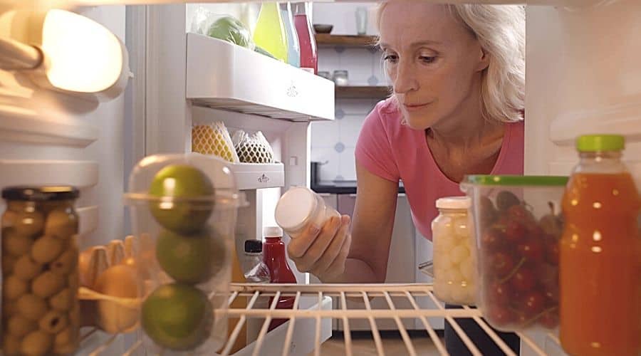A woman checking the contents of her fridge to ensure they are still edible