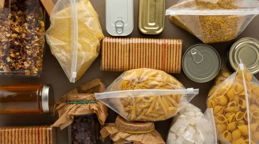 A collection of canned and dry goods, including pasta and grains in zipped plastic bags