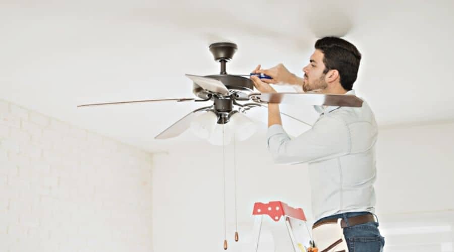 An electrician working on a ceiling fan in a white room
