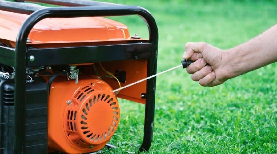 Someone pulling the start cord of an orange generator on a green lawn