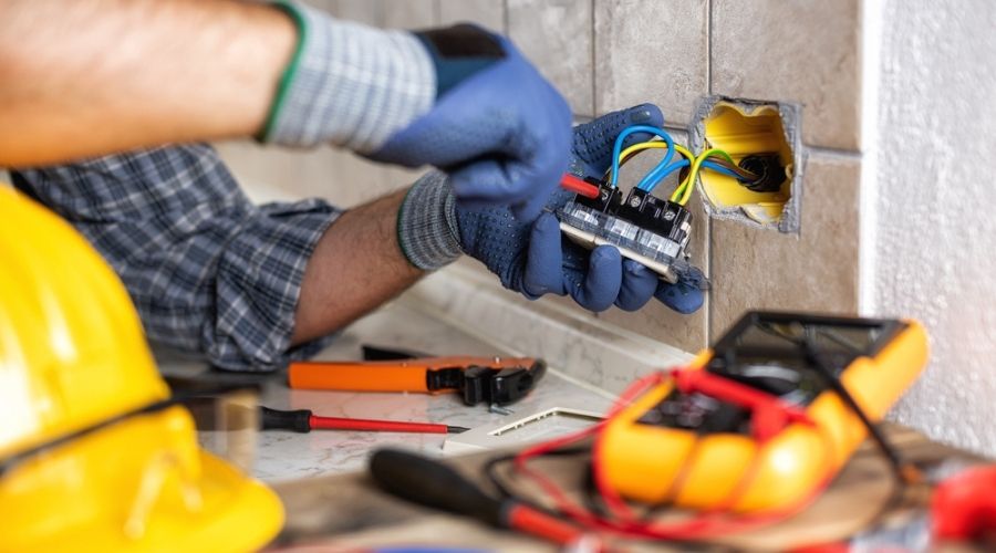 An electrician working on an electrical outlet in a tile wall