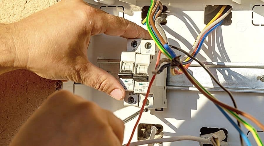 An electrician working on a circuit breaker with multicolored wires pulled out from the panel