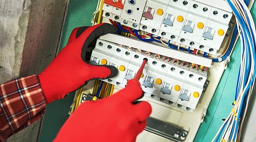 An electrician with red gloves using tools to work on a white circuit breaker