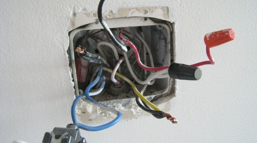 Multicolored electrical wires pulled from a socket in a white wall