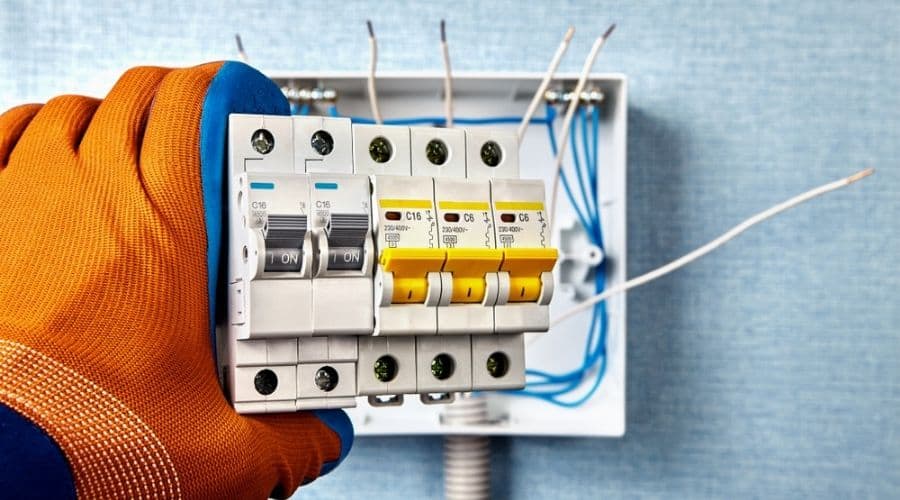 Close-up of a circuit breaker being held by an electrician wearing an orange glove