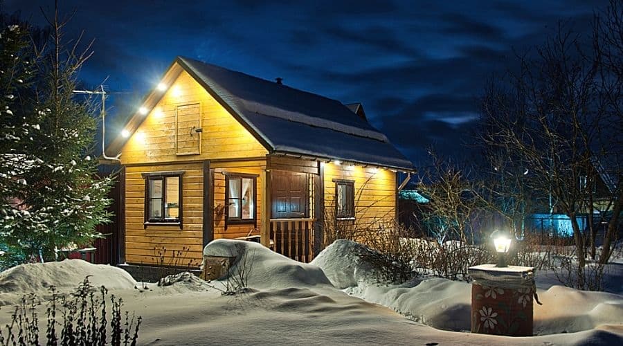 A small house at night in the winter with outdoor lighting