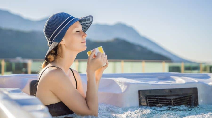 a woman in a hat sips a cup of tea in a hot tub