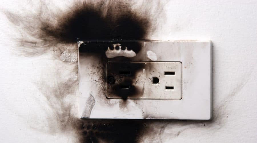 a white electrical outlet shows black smoke damage on the outlet and surrounding wall