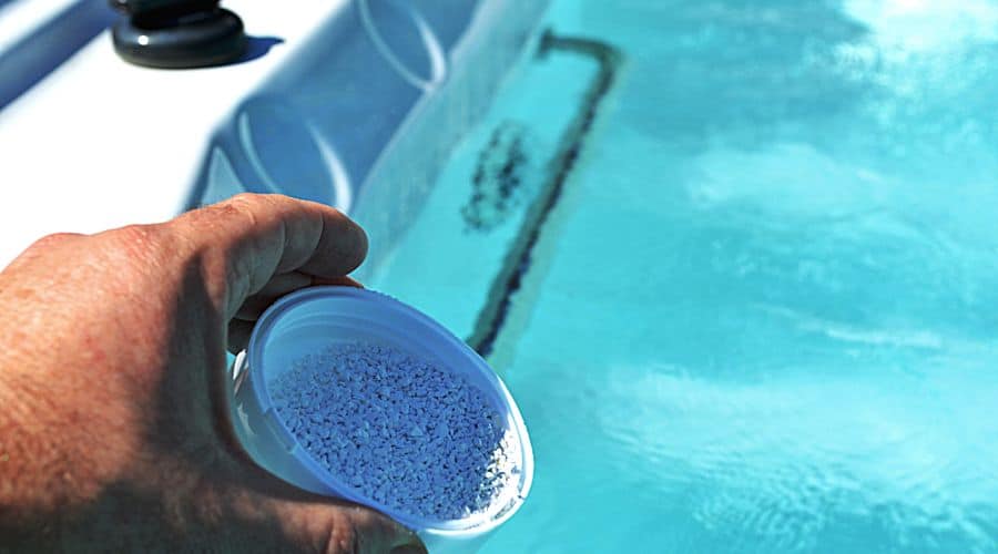 a hand shakes chemical bits into a hot tub
