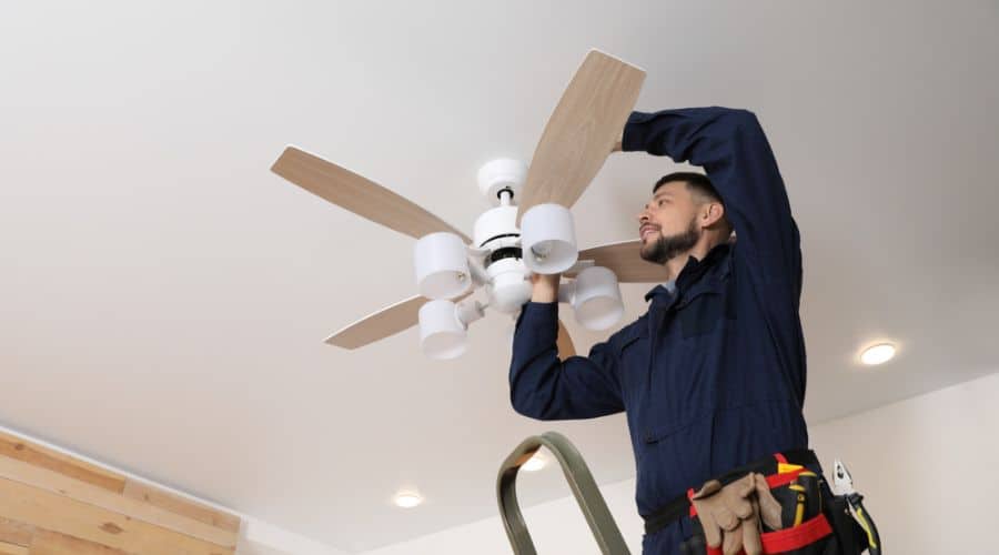 an electrician installs a ceiling fan