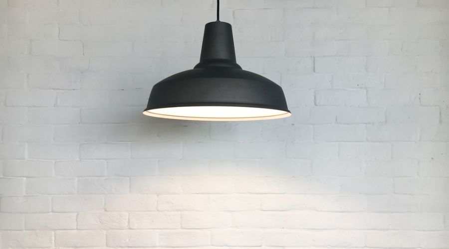 a black drop light fixture against a white brick wall with the bulb turned on